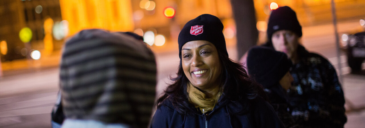 Salvation Army worker talks to person in cool night air.