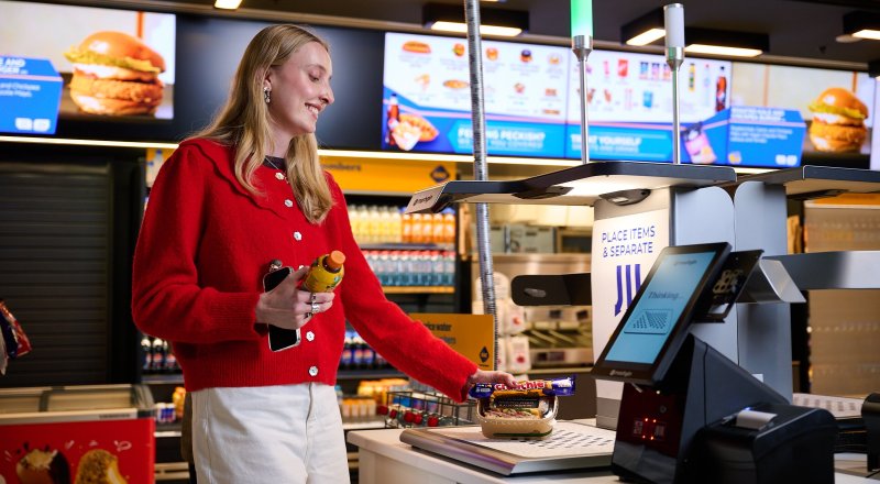 Lady in red cardigan and white pants purchasing food items through the self service checkout at RAC Arena