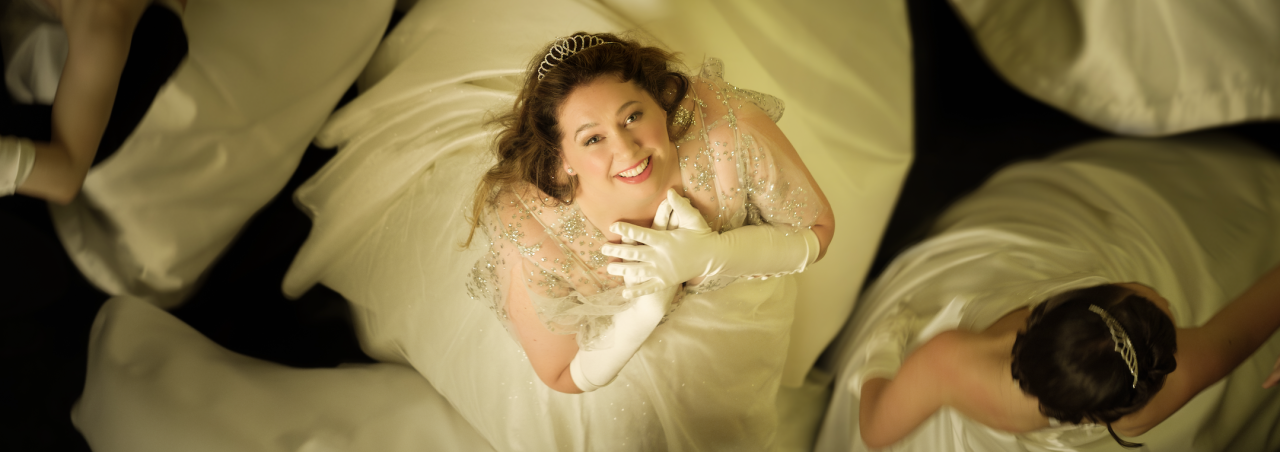 A woman in a bridal outfit for the Deb movie looking above her into the camera with other bride surrounding her