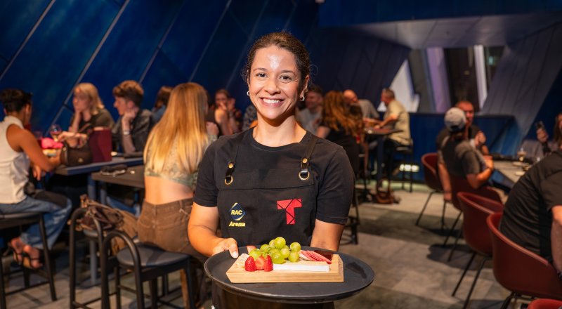 Staff member in The Terrace holding a tray of food with patrons in the background